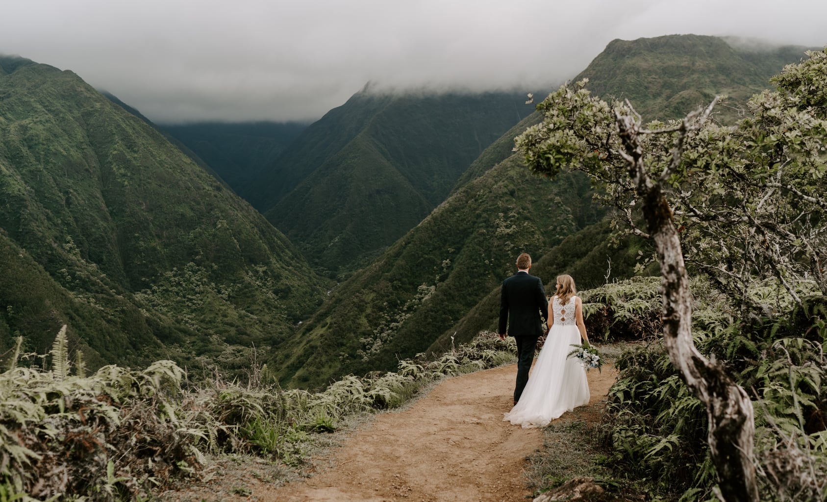 Newlyweds walk along a mountain trail while they elope in Hawaii.