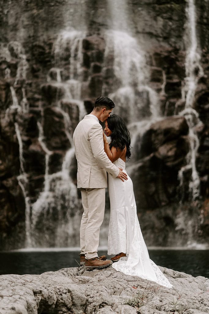 newlyweds hugging in front of a large waterfall during their Big Island elopement.