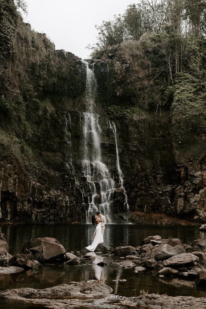 newlyweds standing under a large waterfall during their Big Island elopement.