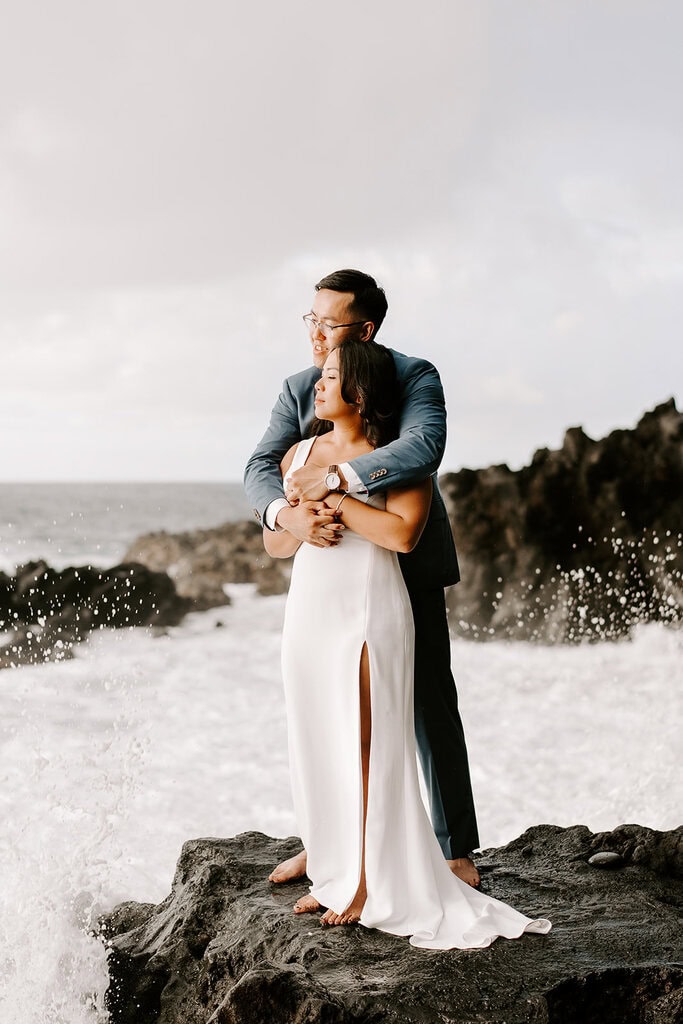 newlyweds hugging on a rugged ocean cliffside.