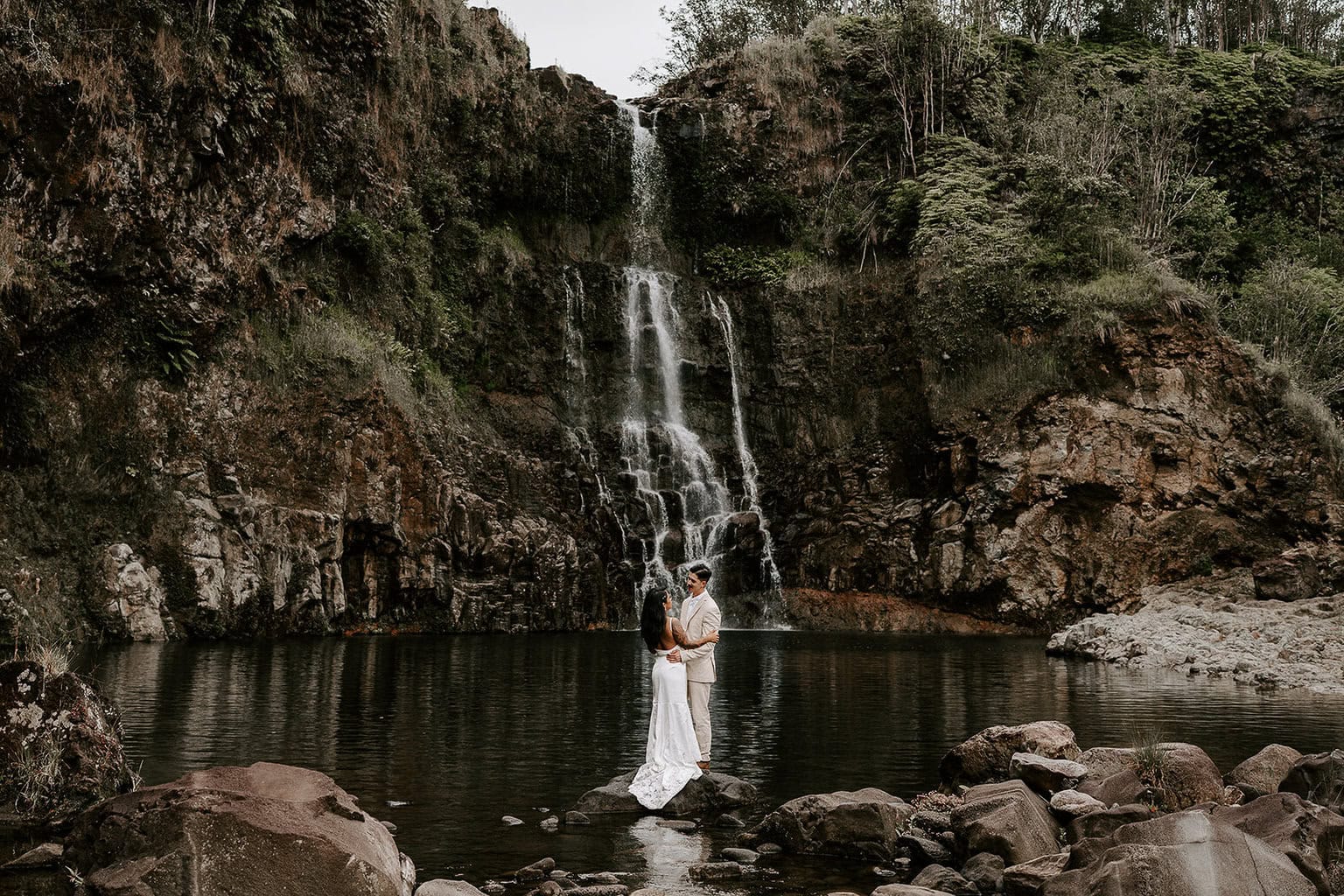 newlyweds holding each other in front of a large waterfall during their Big Island elopement.