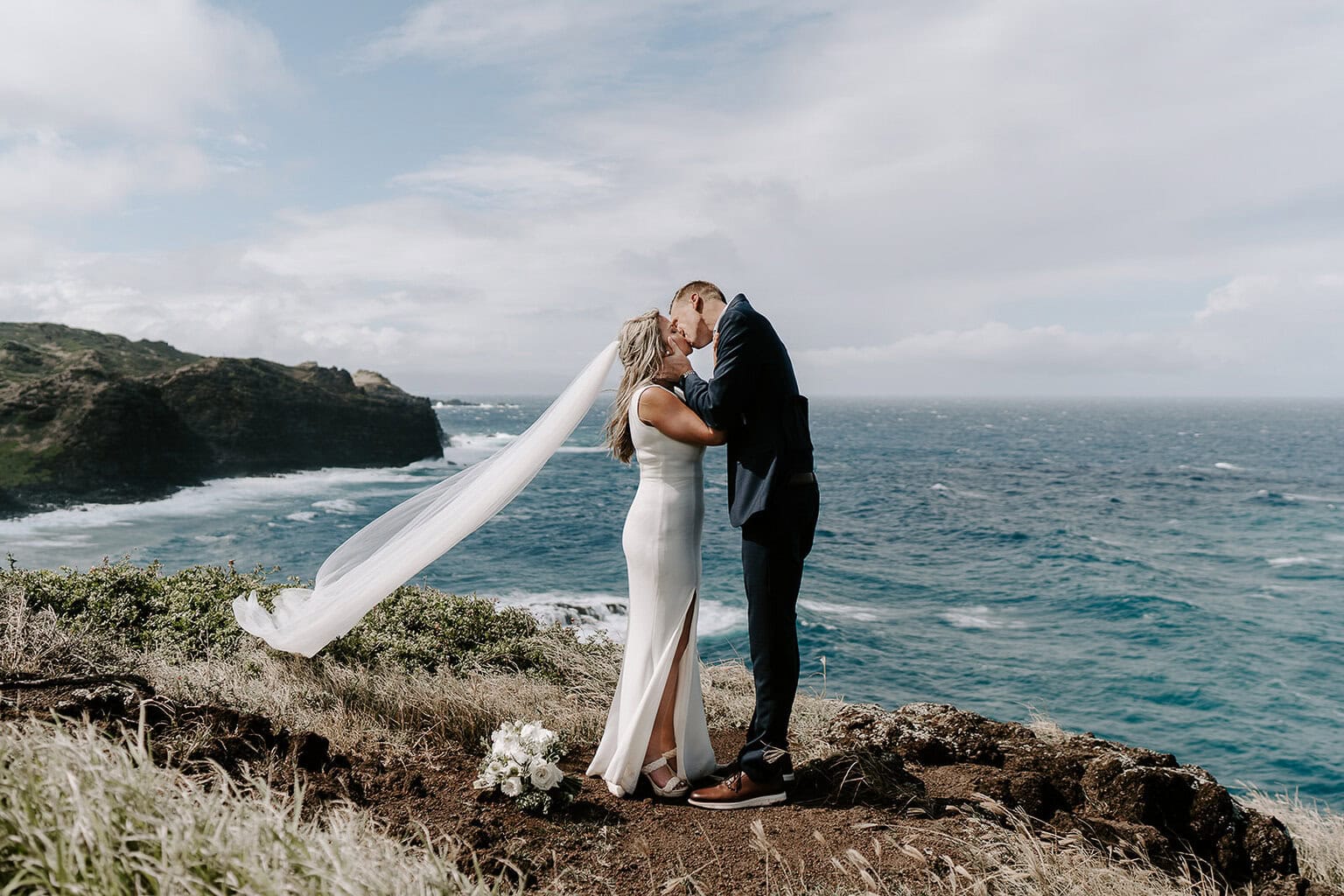 newlyweds kissing on a windy cliffside as they elope in Hawaii.