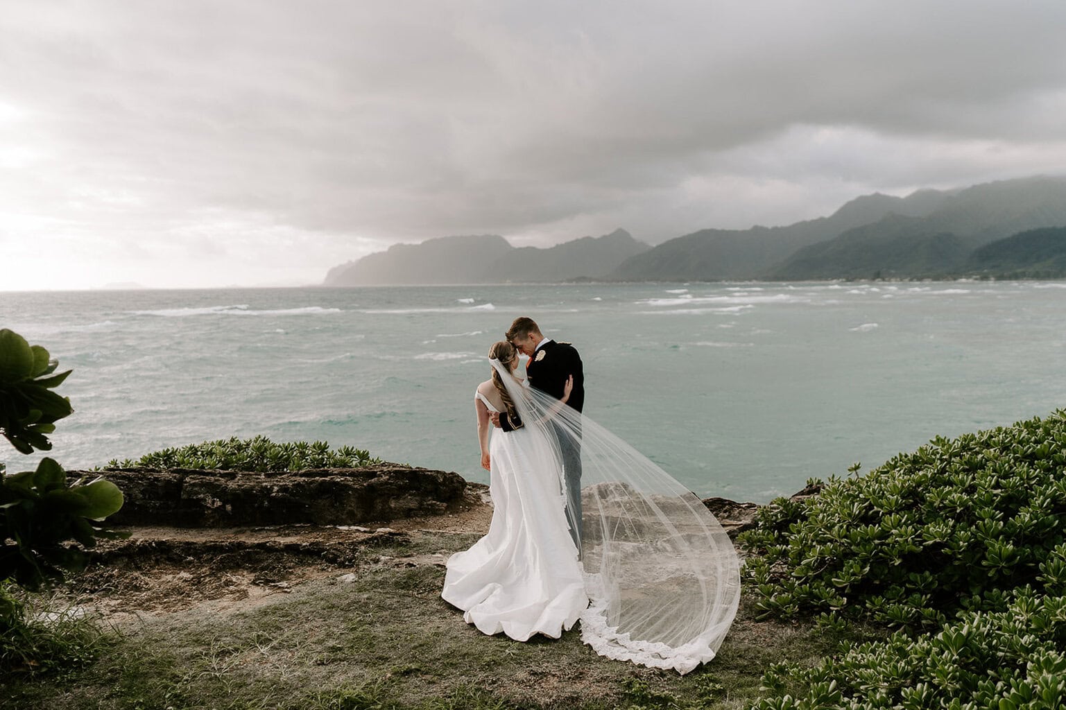 Newlyweds hugging on a cliffside overlooking the ocean during their Oahu elopement.