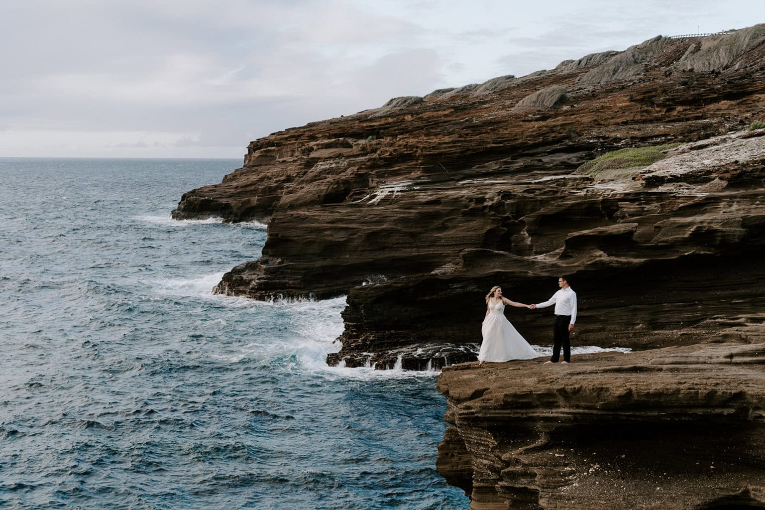 newlyweds holding hands on a cliffside during their Oahu elopement.