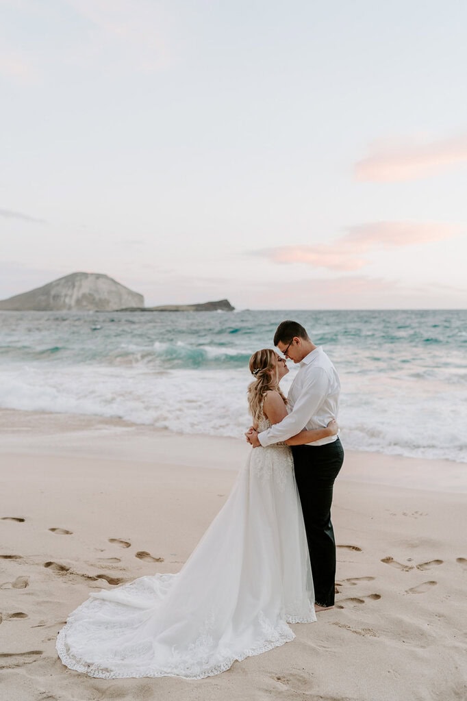 newlyweds hugging on the beach at sunrise.