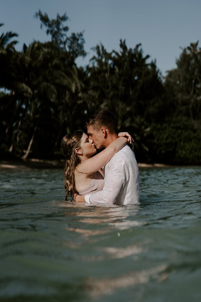 newlyweds hugging and kissing wading in the ocean.