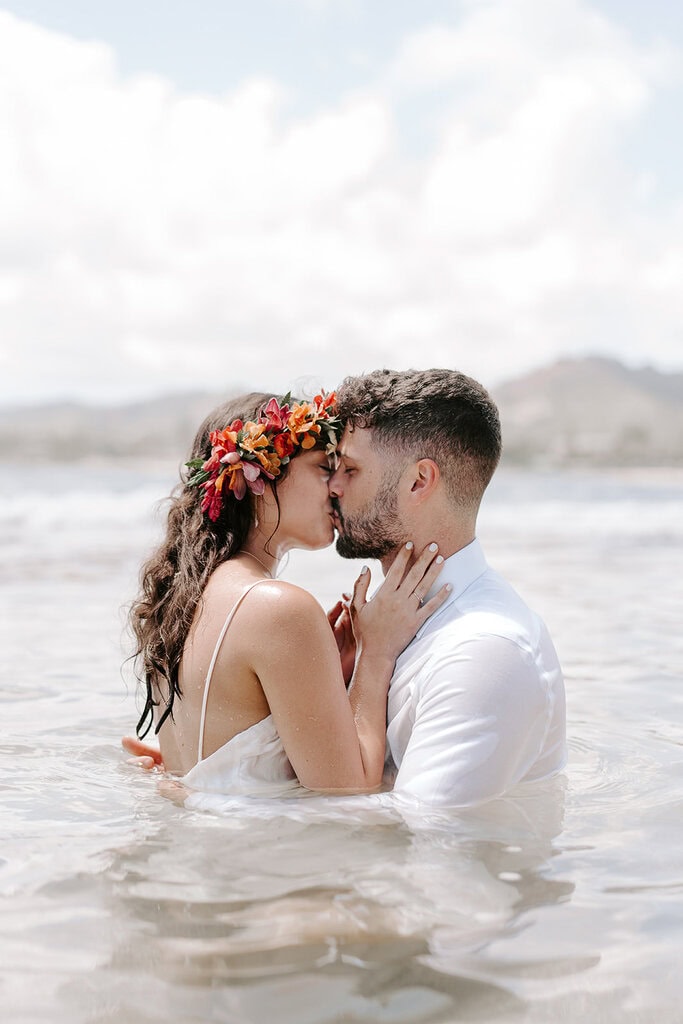 newlyweds kissing while wading in the ocean.