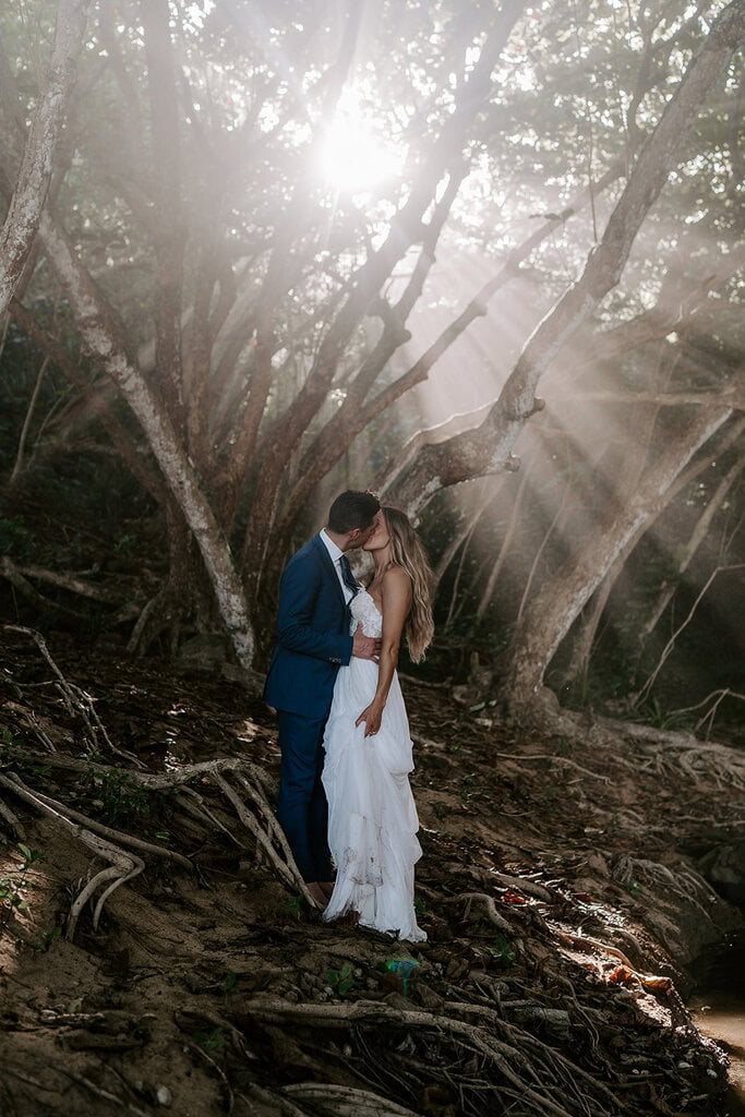 newlyweds kissing in the jungle as the sun peeks through the trees.