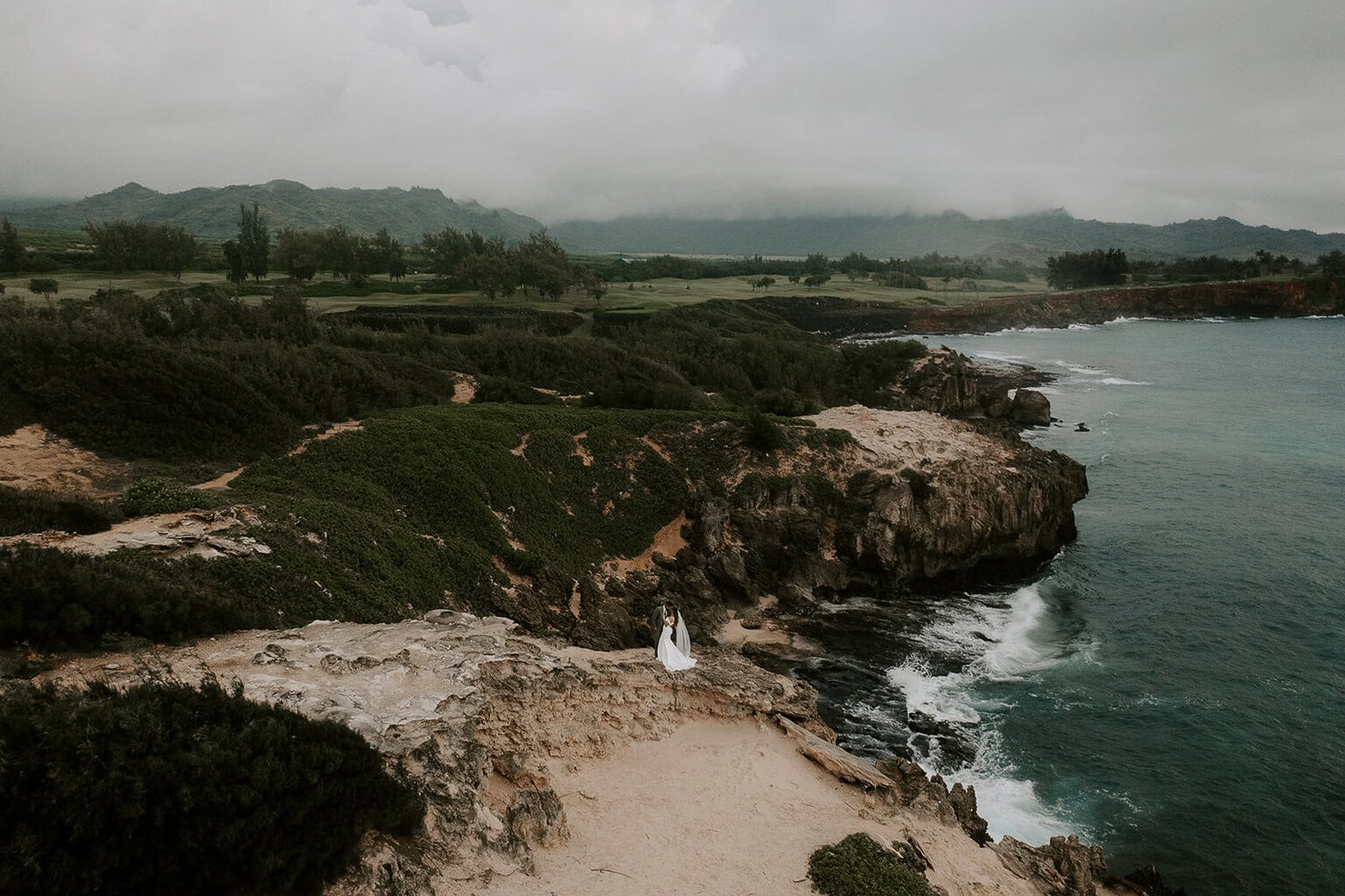 newlyweds standing on a cliffside overlooking the ocean during their kauai elopement.