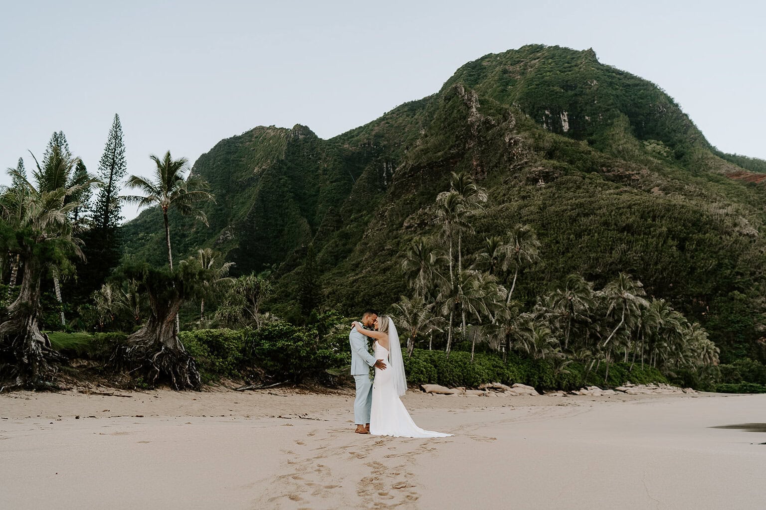 newlyweds hugging on a sandy beach during their kauai elopement.
