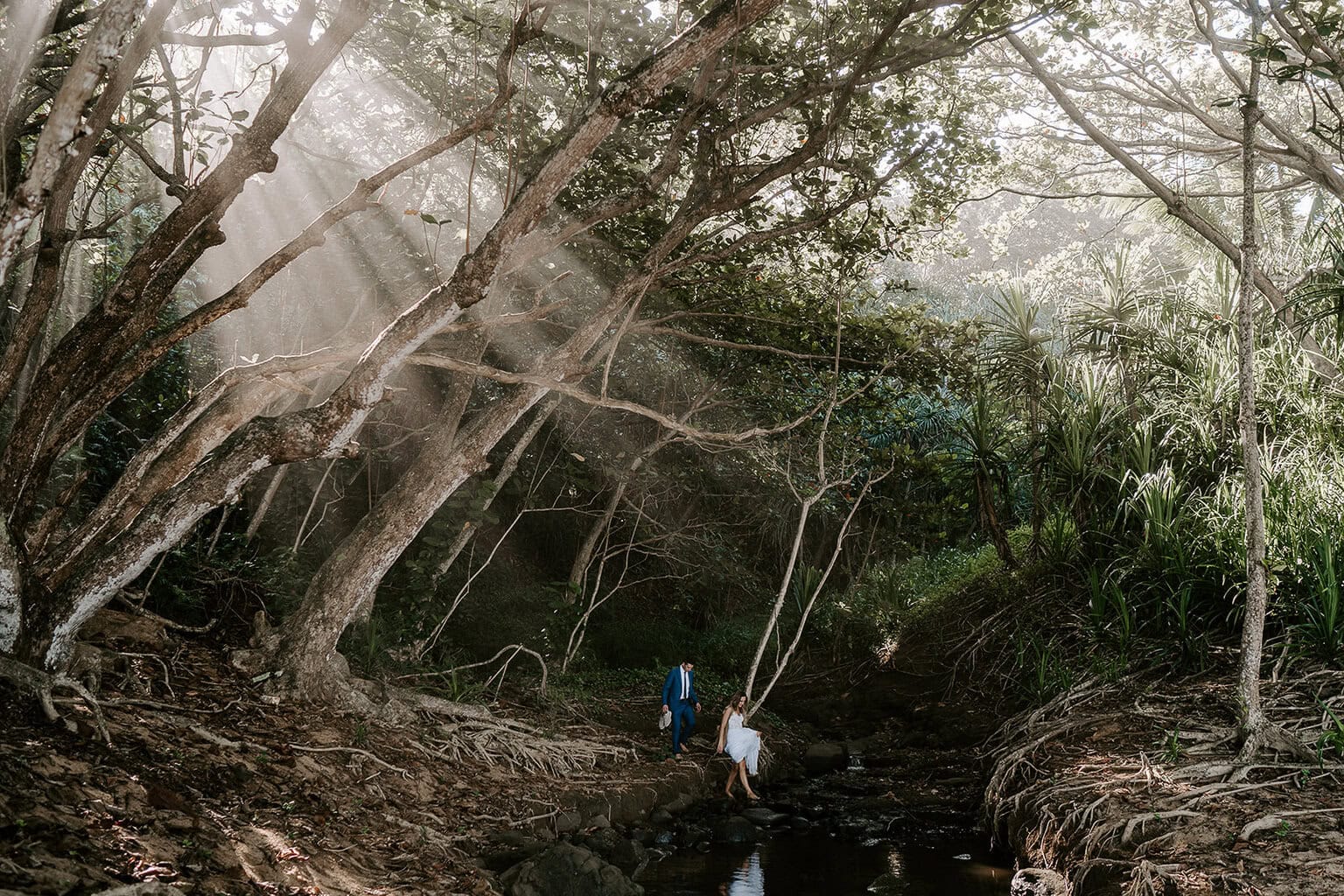 newlyweds walking across a stream in a jungle during their kauai elopement.