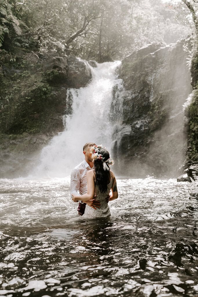 newlyweds kissing in a waterfall during their trash the dress Hawaii session.