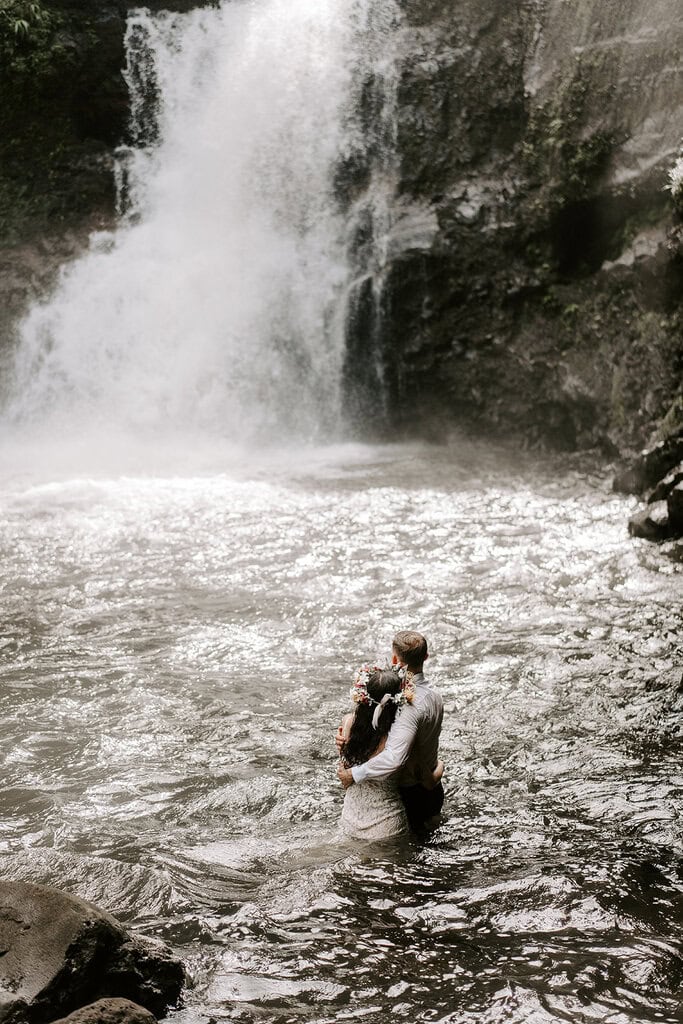 Newlyweds hugging in a waterfall during their trash the dress Hawaii session.