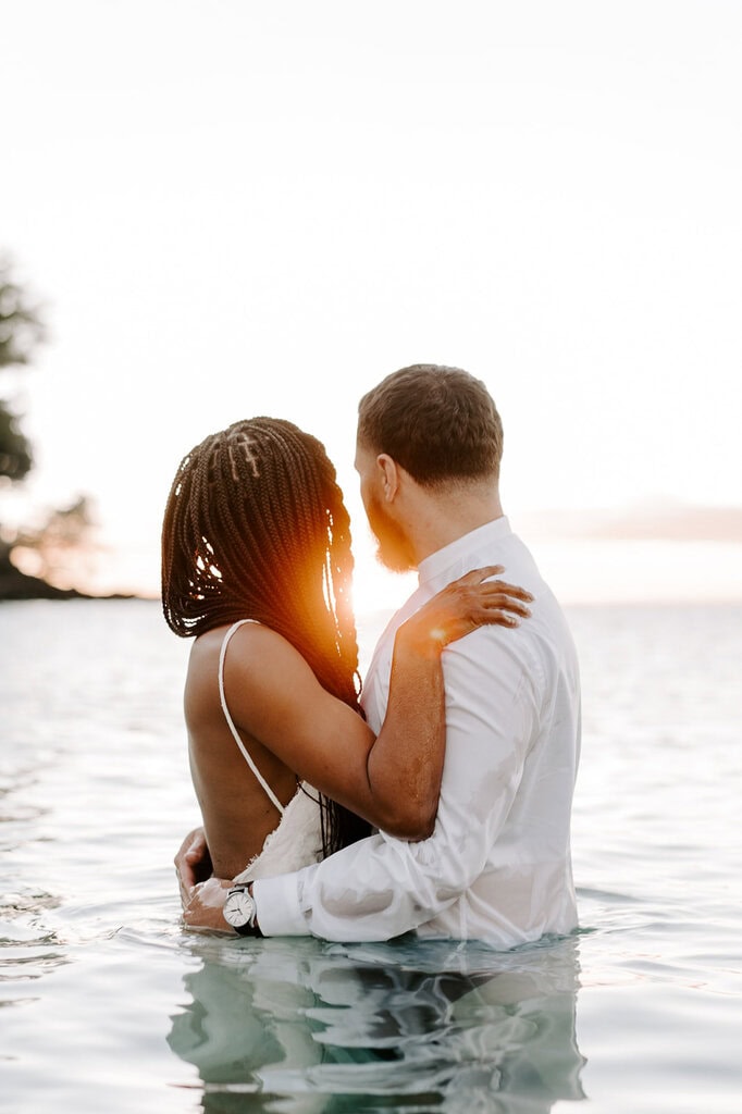 Newlyweds wading in the ocean looking at the sunset during their trash the dress Hawaii session.