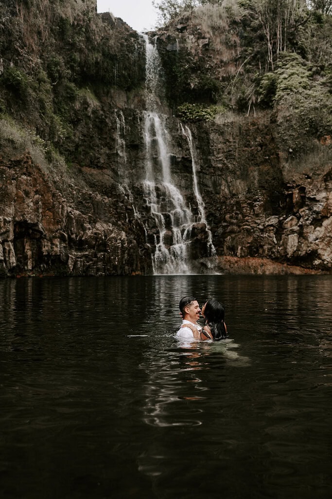Newlyweds wading in a pool in front of a waterfall during their trash the dress Hawaii session.