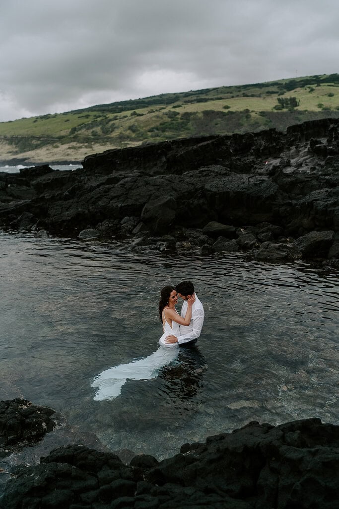 Newlyweds hugging and kissing in a tide pool.