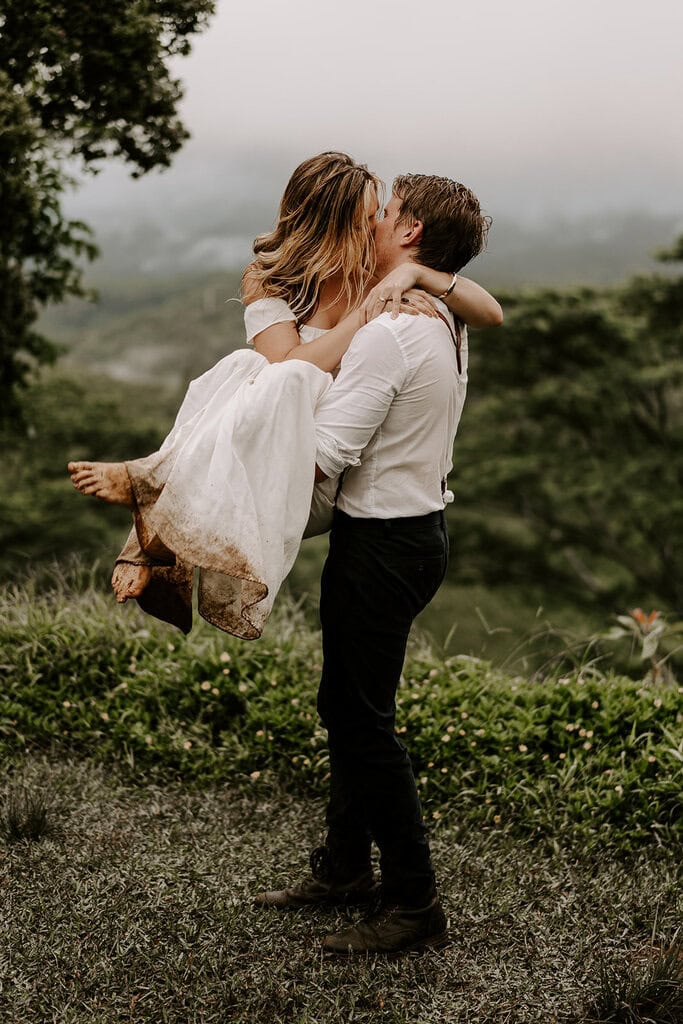Newlyweds kissing while the groom carries his bride wearing a dirty dress during their trash the dress Hawaii session.