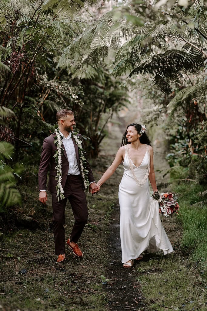 newlyweds holding hands walking though a jungle in Hawaii.