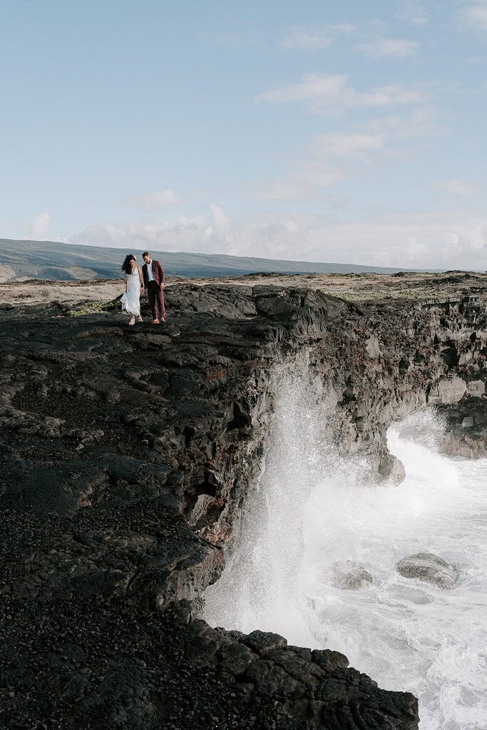 newlyweds standing at the edge of an ocean cliff during their Volcanoes National Park wedding.