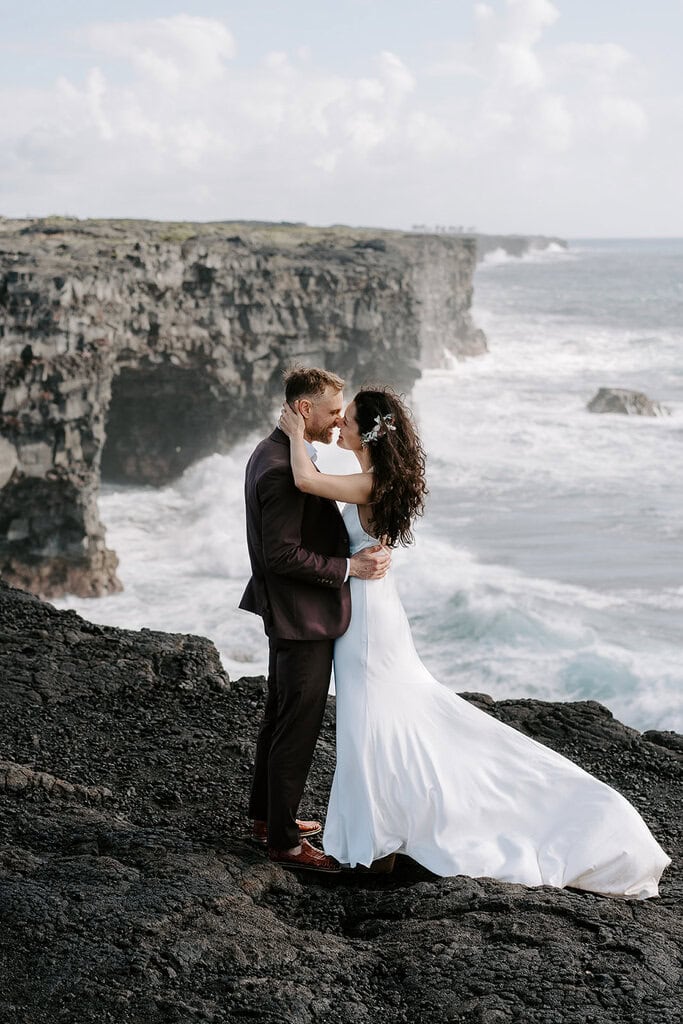 newlyweds kissing at the edge of an ocean cliff during their Volcanoes National Park wedding.