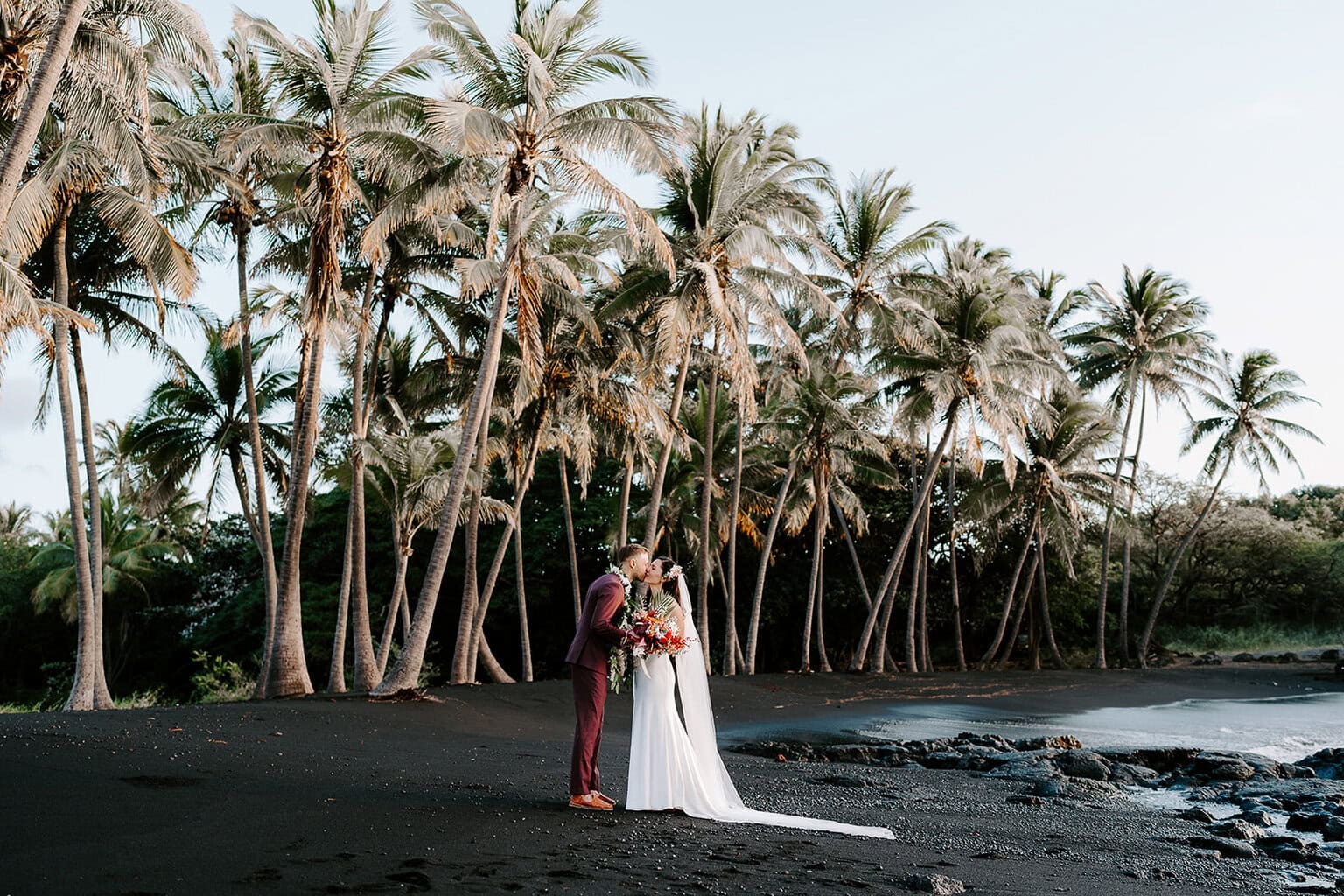 Newlyweds kissing on a black sand beach, one of the best places to get married on the Big Island.
