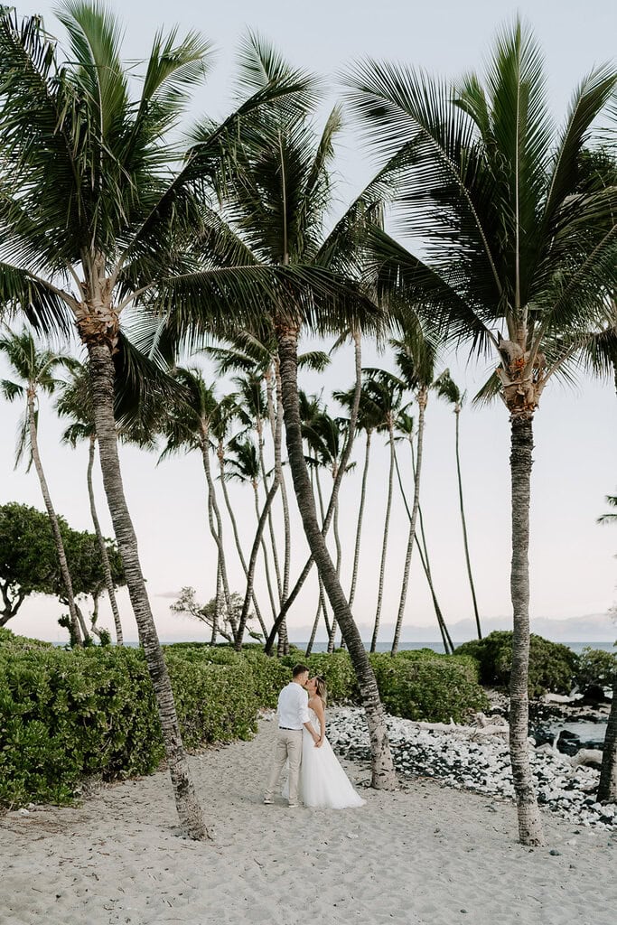 newlyweds kissing standing under coconut trees.