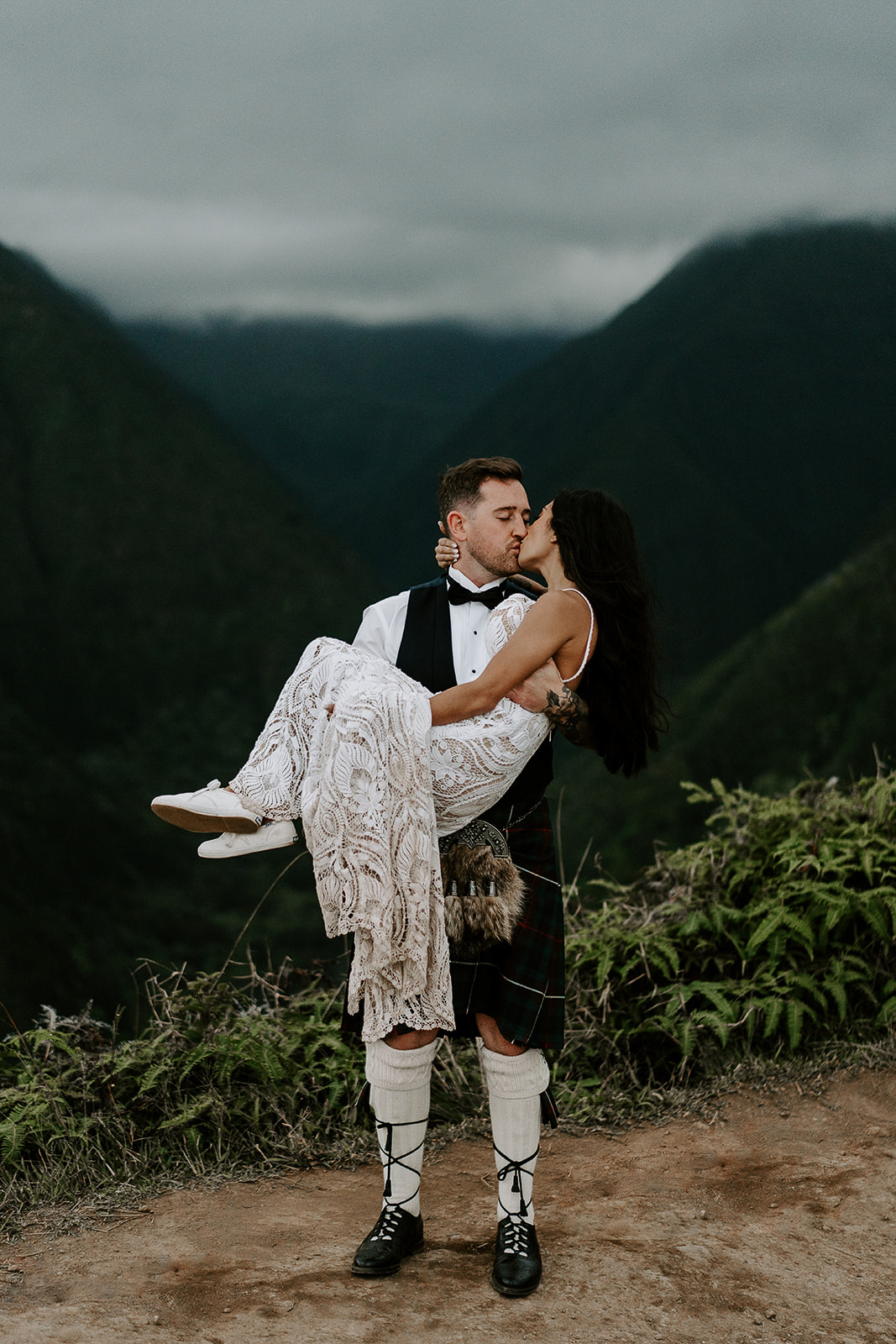 newlyweds kissing while the groom carries the wife next to a green valley, one of the best Maui elopement locations.