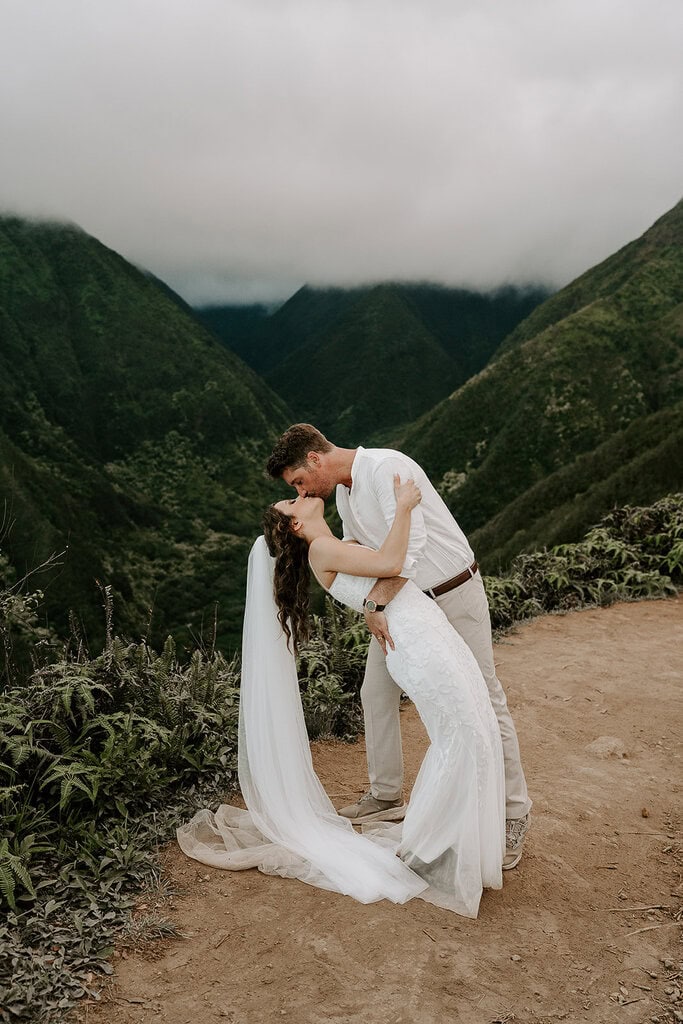 newlyweds kissing on a trail in Maui's green mountains.