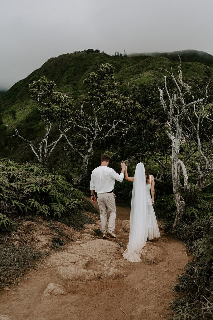 newlyweds hiking down a trail in Maui's green mountains.