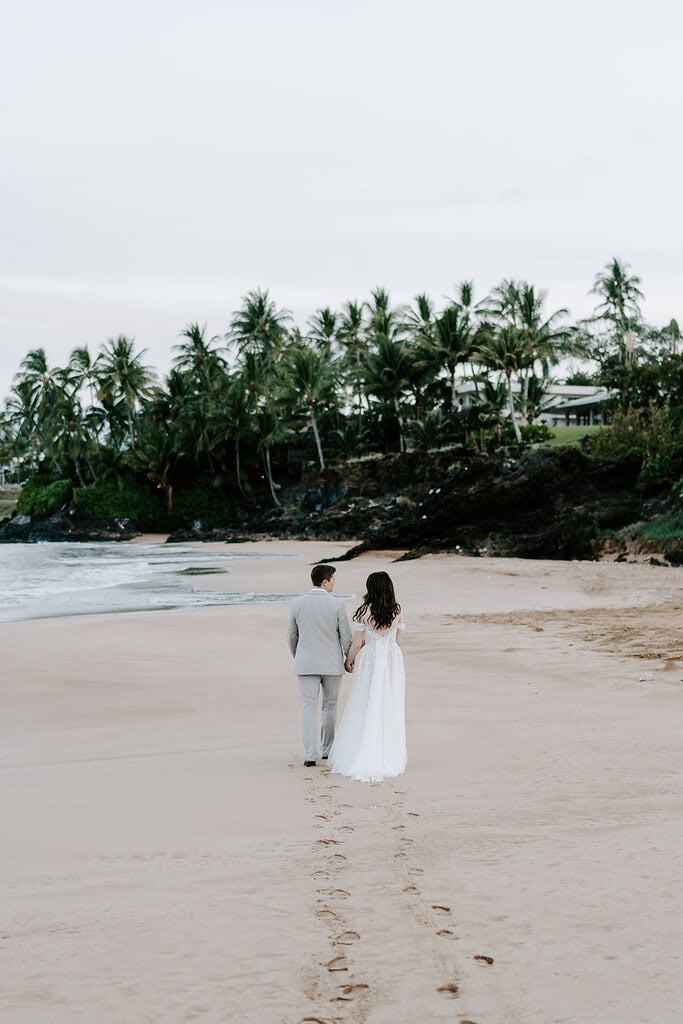Newlyweds holding hands while walking on the beach in Hawaii.