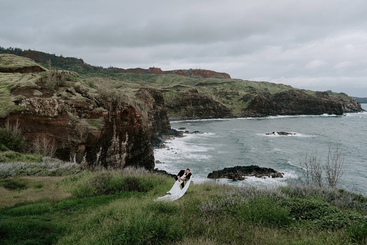 Newlyweds kissing by an ocean cliffside, one of the best Maui elopement locations.