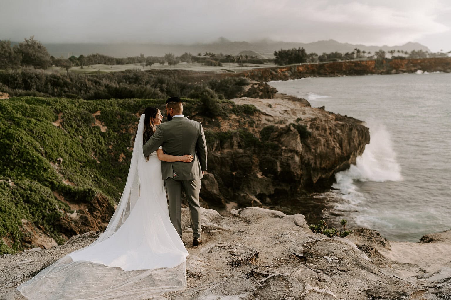 newlyweds hugging on an ocean cliffside in Kauai.