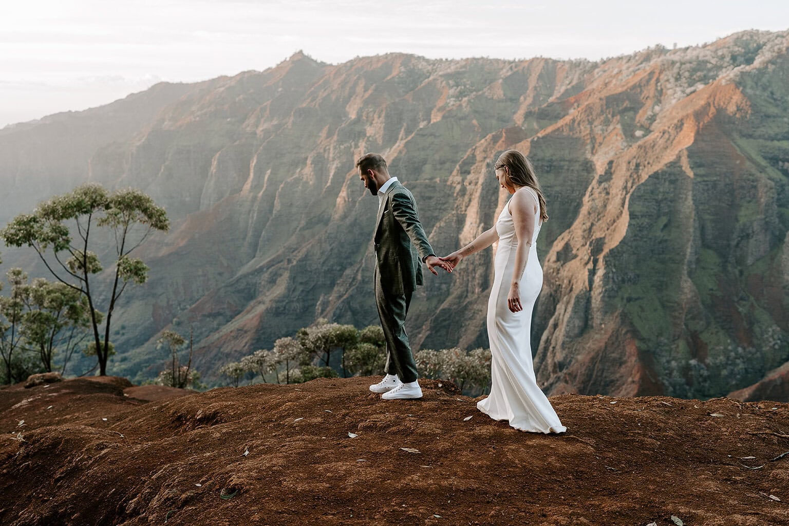 Newlyweds walking along the edge of waimea canyon in their wedding attire.