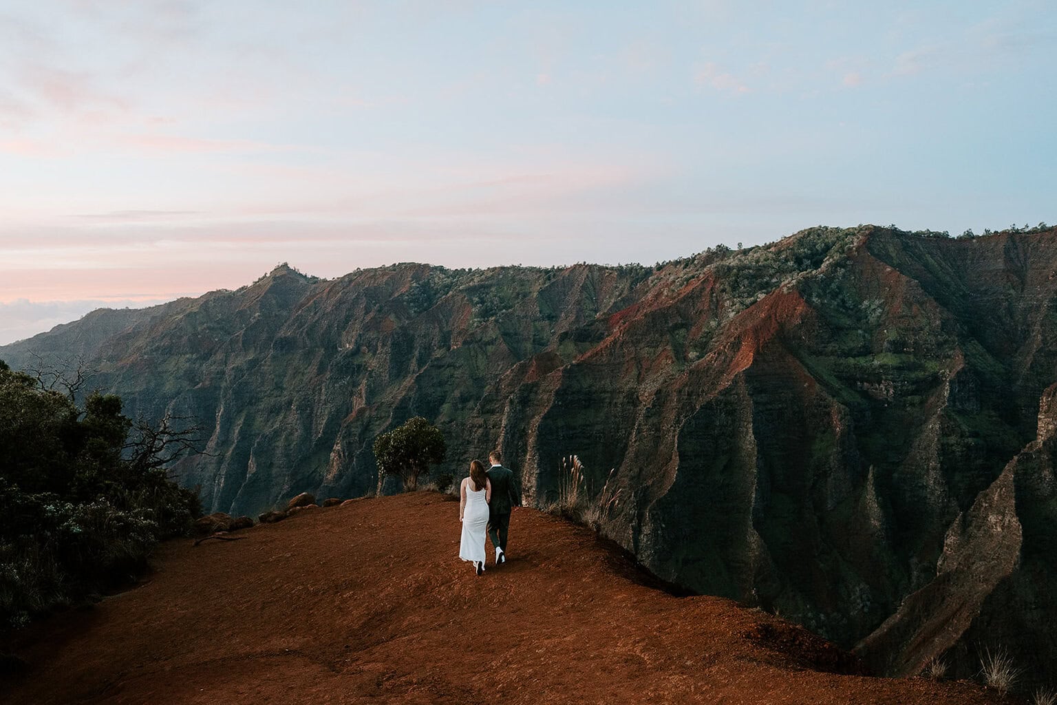 Newlyweds walking toward the edge of the canyon rim as they elope in Waimea Canyon